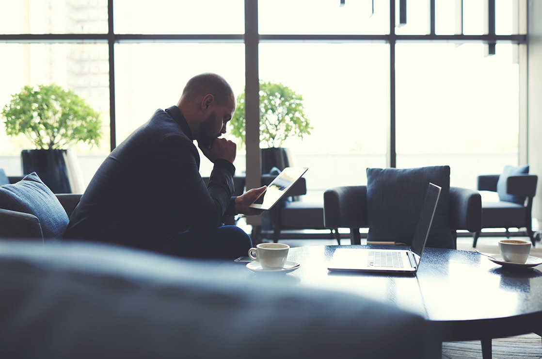 Concerned Man Sitting On Couch Reading His Tablet