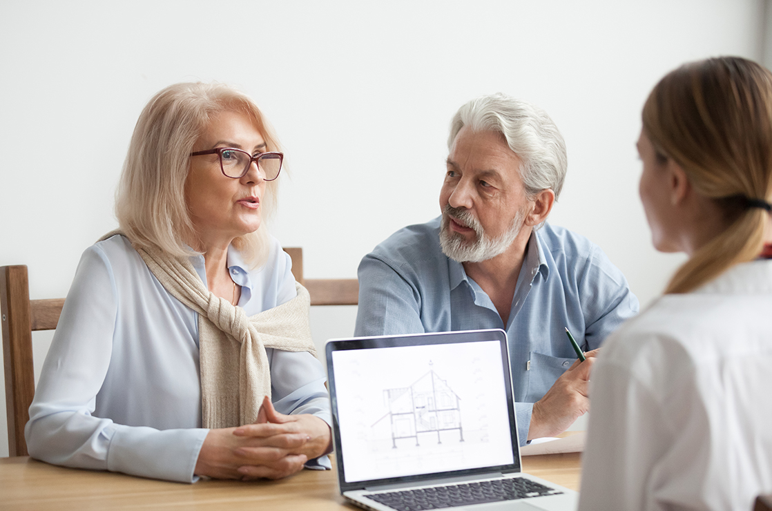 Man and woman sitting at a table, talking to another woman with an open laptop next to her.