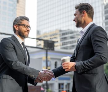 Two 40-50 year old men shaking hands in a business setting smiling