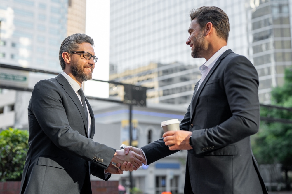 Two 40-50 year old men shaking hands in a business setting smiling